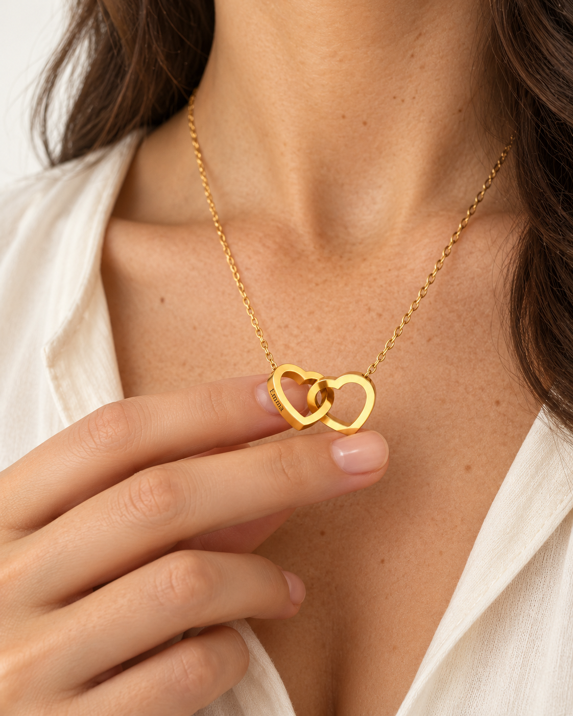 Close-up of the interlocking gold heart necklace held delicately against the chest
